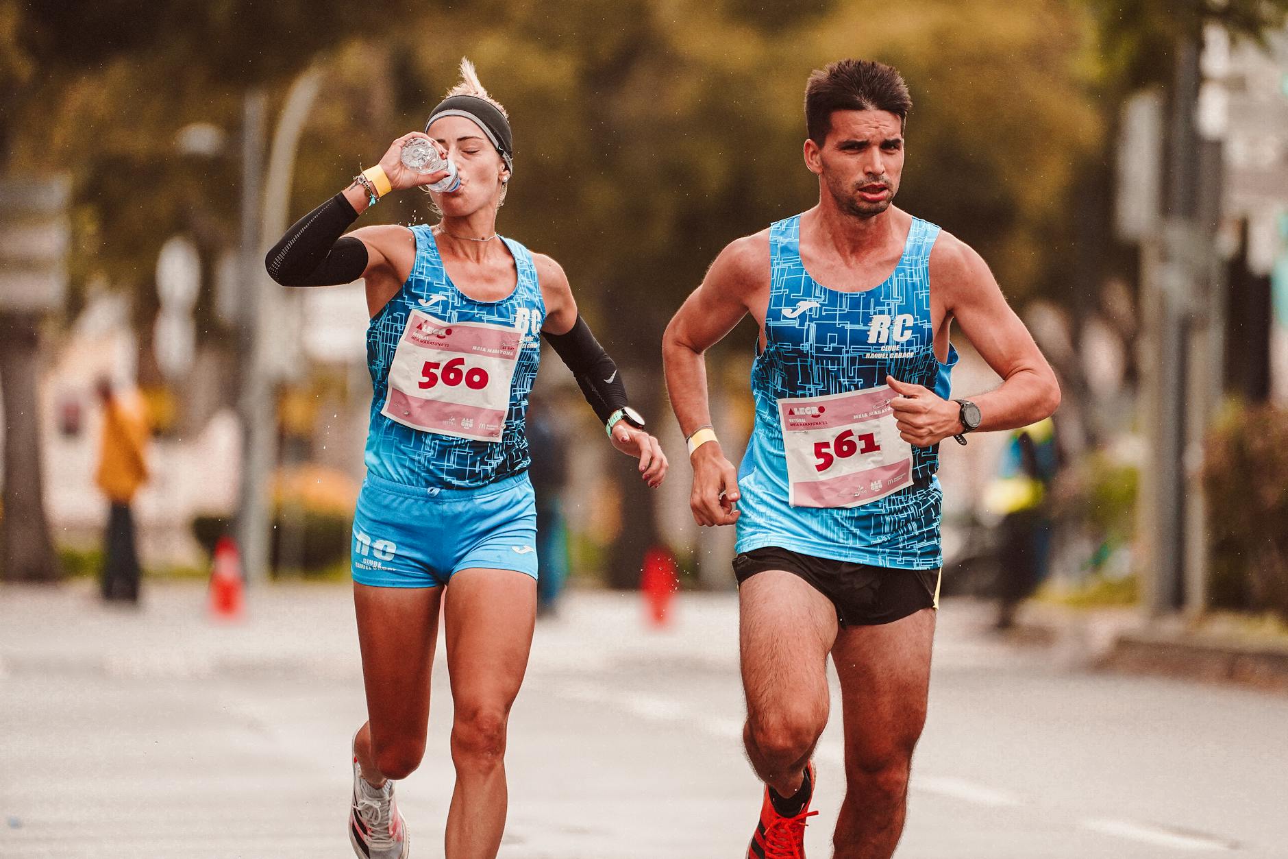 Dwaj biegacze na maratonie piją wodę, biegnąc ulicą miasta